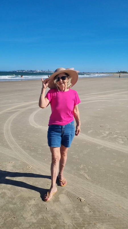 Grécia na praia, de chapéu e blusa rosa.